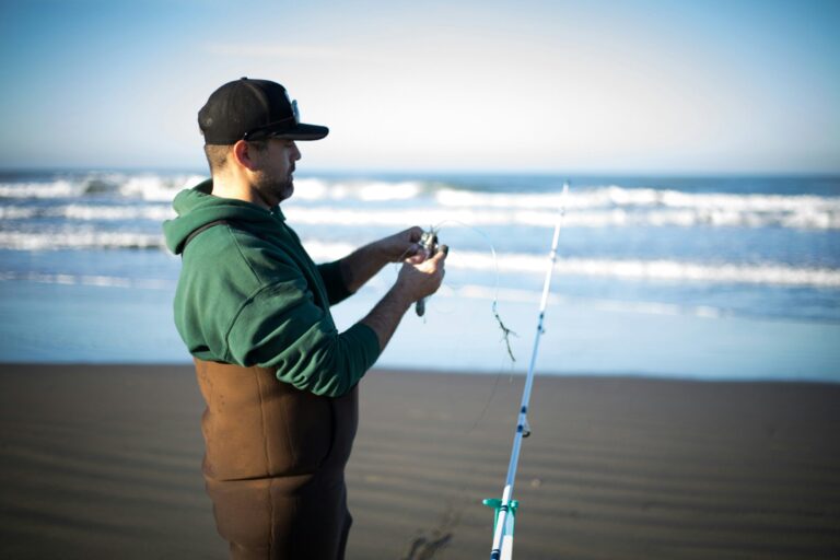 A fly fisherman standing in a shallow river wearing camo chest waders and casting a line